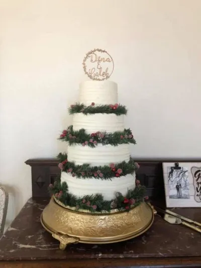 four-tiered christmas wedding cake with evergreen decor and berries